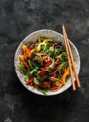 Warm salad with beef, sweet pepper, arugula on a dark background, top view