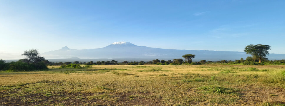 Beautiful panorama view African landscape with mountains and savannah. Kilimanjaro mountain Tanzania snow capped under cloudy blue skies captured whist on safari in Africa Kenya.