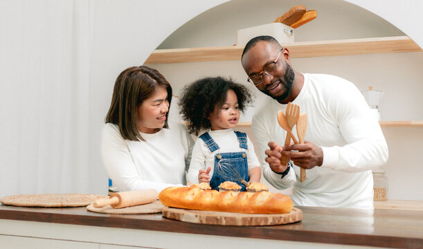 Happy multiethnic family mother father and child having fun playing in cozy kitchen together at home. Playful biracial daughter embracing bonding with dad and Asian mom. Diverse of multiracial people