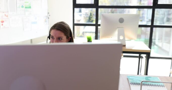 Operator wearing headphones communicates during video conference in office