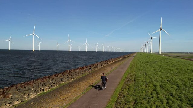 a young man on an electric green bike bicycle by a windmill farm windmills in Netherlands Flevoland Noordoostpolder, men bicycle countryside lake Ijsselmeer on ta Dutch dike