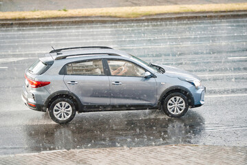 Car driving through the rain on city road - handling wet roads, puddles, and hail safely. Car driving on flooded road, safe and confident car driving in wet conditions. Dangerous driving