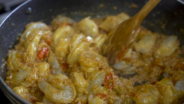 A person uses a wooden stick to stir prawn curry, offering a close-up view of the delicious meal in a dish, embodying the concept of culinary expertise.