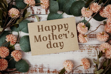 Happy Mother's Day text message on paper card with flowers border frame on wooden background