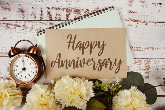 Happy Anniversary text message on paper card with flowers border frame on wooden background