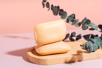 Two bars of soap in a wooden soap dish with dried flowers against a pink background.