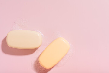Two bars of soap with foam on a pink background.
