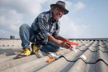 Homeowner or technician man repaired the house himself, protected the roof by applying sealant to cover rain leaks with a brush, on the roof of his house