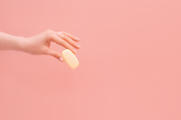 Female hand holding a bar of soap against a pink background.