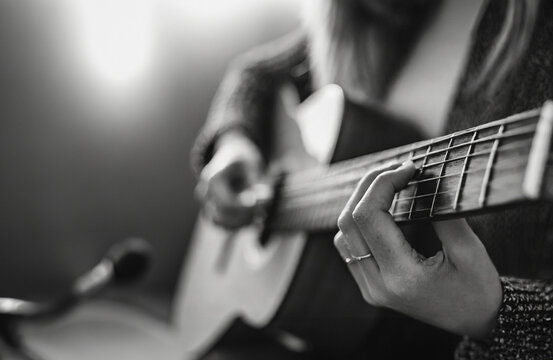 A female musician plays an acoustic guitar while recording at a studio into a microphone - the camera focuses on her fingers and the fretboard and the body of the guitar is in soft focus, live concert