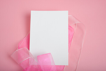 Blank postcard next to a pink ribbon on pink background. Mockup.