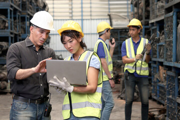 Asian woman worker with safety vest and helmet holds laptop, reports information to her supervisor...