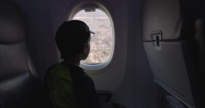 Young boy looking out airplane window flying over city