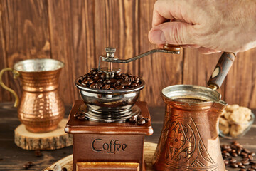 Grinding coffee beans into a vintage coffee grinder, coffee maker and copper cup on a wooden...