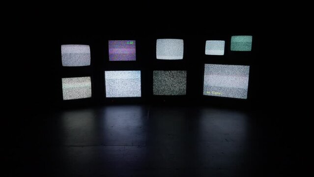 A wall of assorted old cathode televisions in a dark and isolated room.