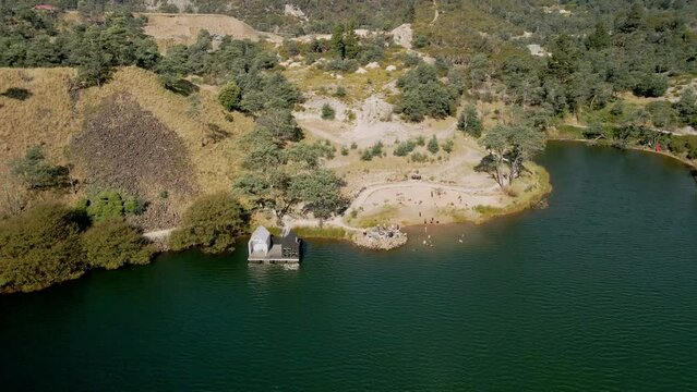 Reverse aerial of Derby Lake Floating Sauna with tourists swimming at beach, in Derby, Tasmania, Australia