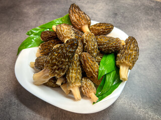 Fresh raw edible and tasty morel mushrooms with green bear garlic leafs on white plate