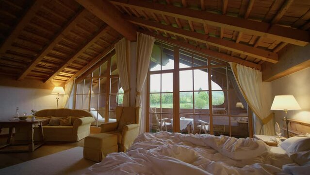 Empty hotel room in the mountains with undone bed. Large room with cozy furniture with a large balcony.