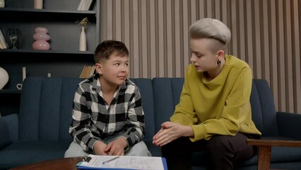 Caring positive pretty female psychologist talking with upset adorable preadolescent African American boy, helping to overcome mental problems and improve social skills during psychotherapy session.