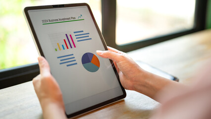 Action of a person hand is touching on tablet screen to review the 2024 business investment plan with graph and chart data. Business working with technologyo concept, close-up and selective focus.
