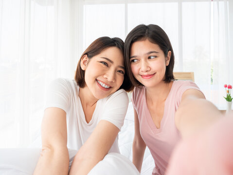 A pair of Asian young women sharing a moment of joy as they take a selfie in a light filled cozy room with a warm and friendly ambiance
