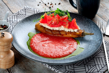 Baked eggplant with cottage cheese and tomatoes in a plate on a wooden background