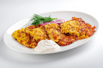 Fried Potato pancakes with sour cream in a white plate on a white background. Grated potatoes fried in oil