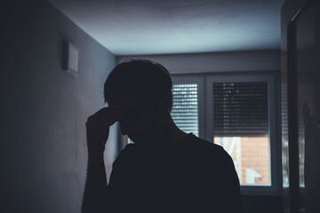 Silhouette of depressed sad man in dark room with window shutters pulled down - obrazy, fototapety, plakaty