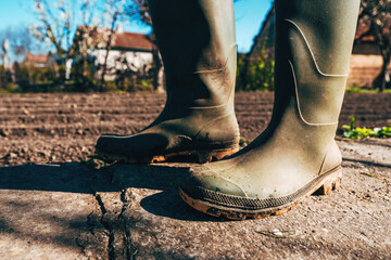 Closeup of dirty rubber boots, gardener posing in organic garden