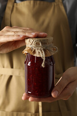 Glass jar with fig jam in female hands on light background, close up