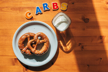 Carbs for breakfast concept, glass of yogurt and two pretzels on a plate on the table in the morning