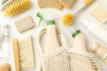 Eco bag, bottles with detergents and cleaning tools on light background, top view