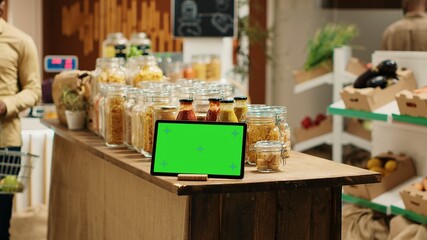 Greenscreen display shown on tablet at neighborhood grocery store, support low carbon footprint and eco friendly farming. Gadget with blank copyspace layout next to bulk items in jars. Camera 1.