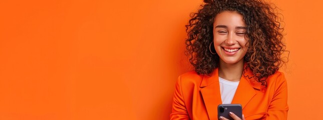 Portrait of smiling african american woman using smartphone isolated on orange background, wearing...