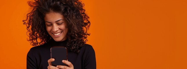 Portrait of smiling african american woman using smartphone isolated on orange background, wearing red sweater with copy space for your text message or promotion banner.