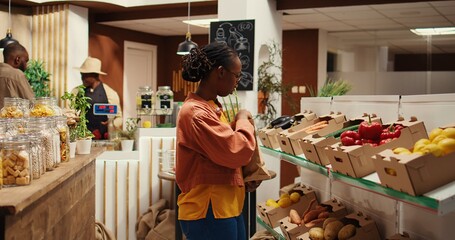 Vegan person searching for freshly harvested vegetables from crates, shopping for natural groceries at local zero waste eco store. African american client looking at organic food items. Camera 2.