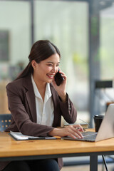 Asian businesswoman Company sales manager while talking on the phone with a customer, looking at documents, files, financial details, agreements, and business contracts on a laptop in the office.