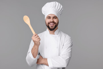 Happy young chef in uniform holding wooden spoon on grey background