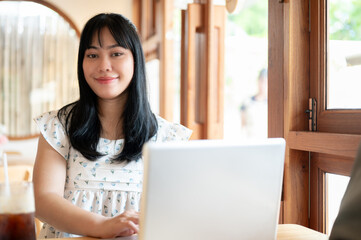 A beautiful young Asian woman sitting in a coffee shop with her laptop computer, working remotely.