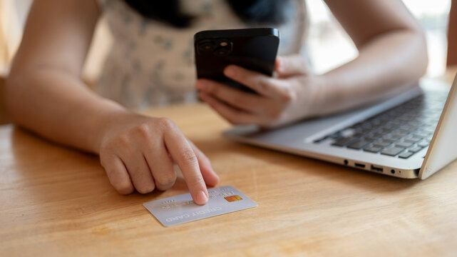 A close-up image of an Asian woman pointing her finger at a credit card on the table.