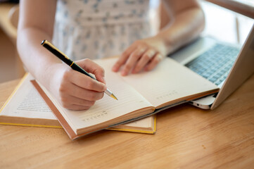 A close-up image of a woman holding a pen, writing something in a notebook or keeping diary.