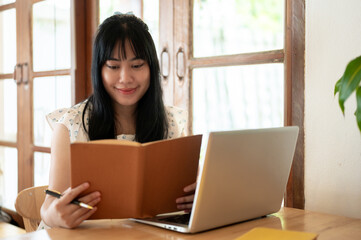 A beautiful young Asian woman is focusing on reading a book, working remotely at a coffee shop.