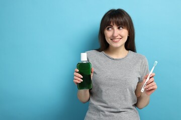 Young woman with mouthwash and toothbrush on light blue background, space for text
