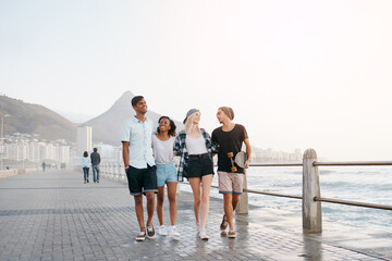 Group, friends and walk on promenade by ocean with smile for diversity, bonding and space for mockup. Men, women or gen z people with conversation, happy and outdoor on boardwalk by sea for vacation © peopleimages.com