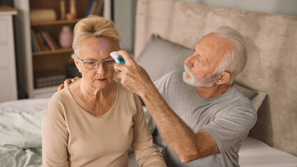 An elderly couple measuring temperature with thermometer in bedroom