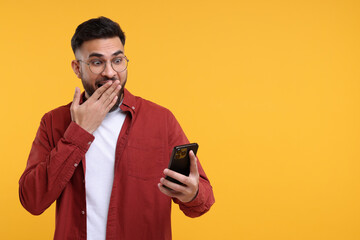 Emotional young man using smartphone on yellow background, space for text