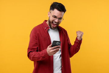 Happy young man using smartphone on yellow background