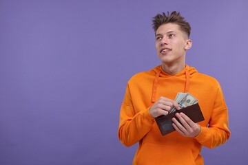 Happy man putting money into wallet on purple background. Space for text