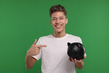 Happy man pointing at piggy bank on green background