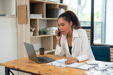 Young professional woman engaged in a phone conversation while working on her laptop at an organized office desk.